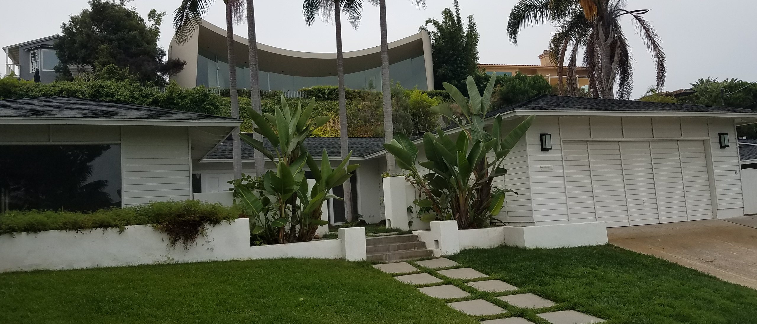 Hillside residential grade in La Jolla — white lap-sided house, retaining walls, and palm trees. Local-context view, not a La Jolla Structural project.